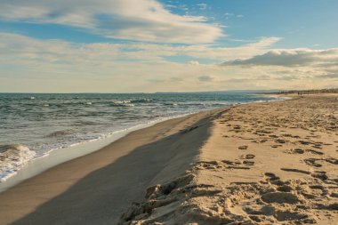 İzleri ve ayak izleri olan güzel sarı kumlu sahil turkuaz deniz kenarında güneş ışığı ve dalgalar.