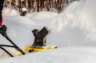 Man is brushing white snow with the yellow electric snow thrower in a winter garden clipart