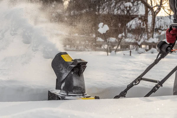 L'uomo sta spazzolando la neve bianca con il lancianeve elettrico giallo in un giardino d'inverno — Foto Stock