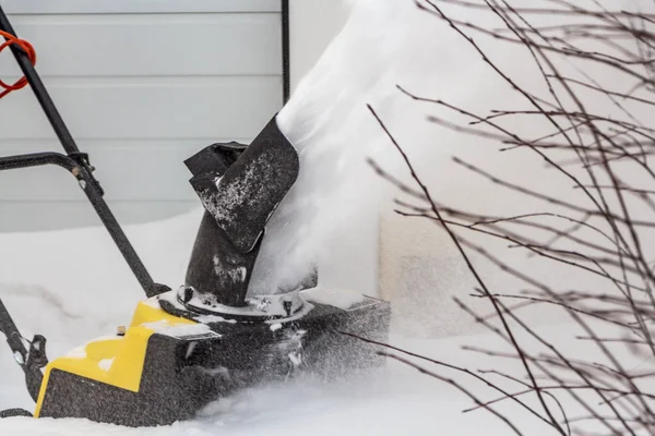 De mens poetst witte sneeuw met de gele elektrische sneeuwwerper in een wintertuin — Stockfoto