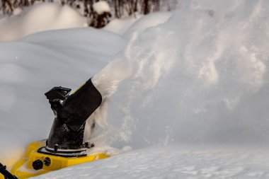 İnsan, kış bahçesinde beyaz karı sarı elektrikli kar makinesiyle fırçalıyor.