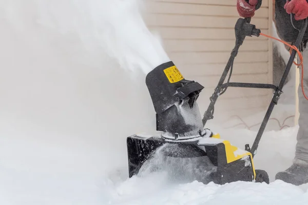 De mens poetst witte sneeuw met de gele elektrische sneeuwwerper in een wintertuin — Stockfoto