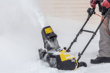 Man is brushing white snow with the yellow electric snow thrower in a winter garden clipart