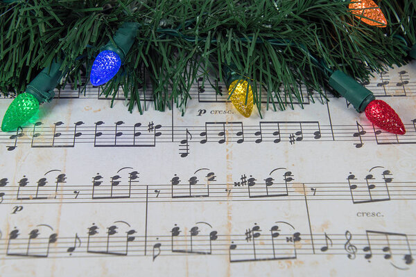 colorful holiday lights and green garland on worn sheet music