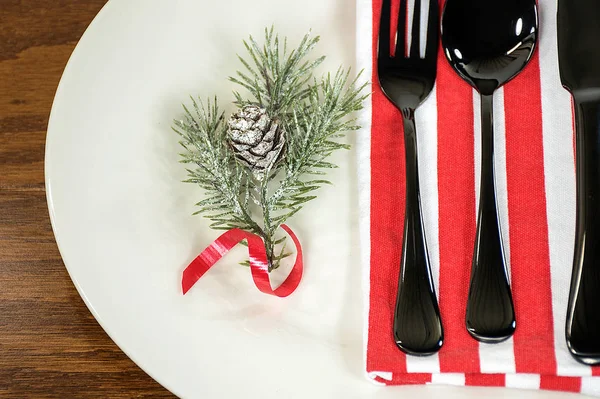 クリスマスの松の枝 木製のテーブルの黒の銀器と白いディナー プレートに赤いリボン — ストック写真