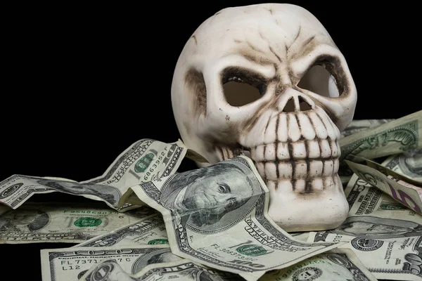 human skull in a pile of American currency on black background