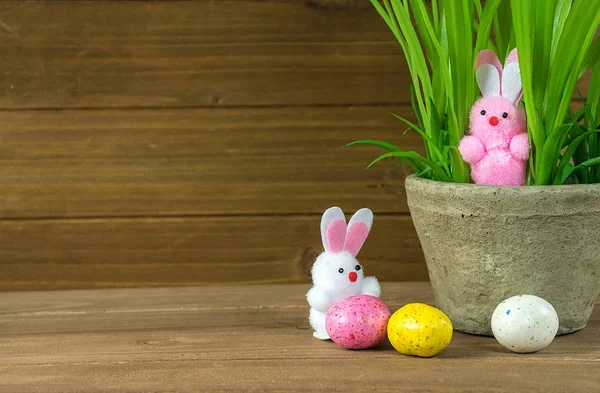 ピンクしお菓子卵とファジィのイースターのウサギを白や木の植木鉢に草 — ストック写真