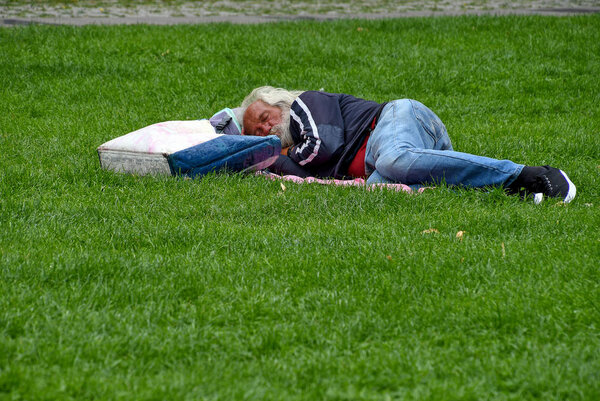 homeless man with bag and blanket sleeping on grass
