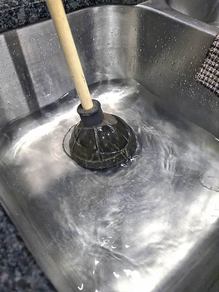 household plunger fixing clogged drain  in stainless steel kitchen sink with water