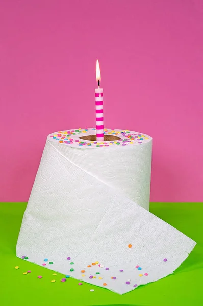 キャンディ コンフェッティと誕生日キャンドルの白いトイレットペーパーのロールを緑とピンクの背景に — ストック写真