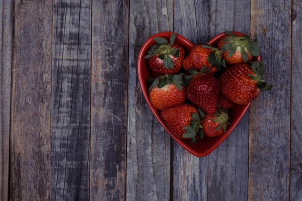 Herzförmige Schale mit Erdbeeren auf hölzernem Hintergrund — Stockfoto