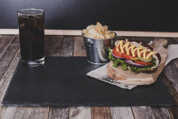 Classic hot dog with chips and drink on dark background.