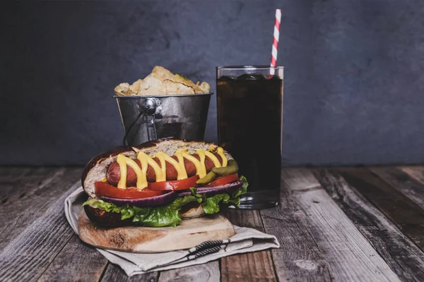 Classic hot dog with chips and drink on dark background.