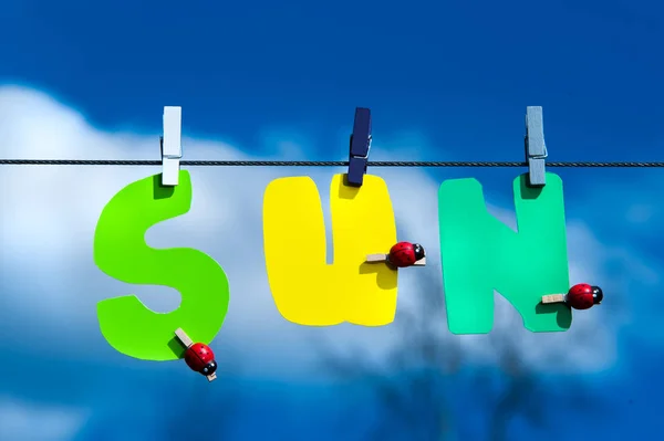 Inschrift Sonne in bunten Buchstaben auf Wäscheklammern am blauen Himmel b — Stockfoto