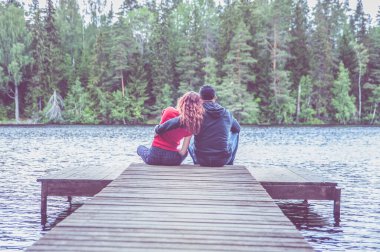 Bir adam ve bir kız güzel bir gölün rıhtımında oturup sarılıyorlar. Aşk kavramı, yaz havası. 