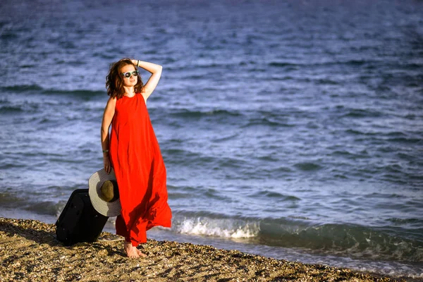 Donna in abito rosso con valigia mare — Foto Stock
