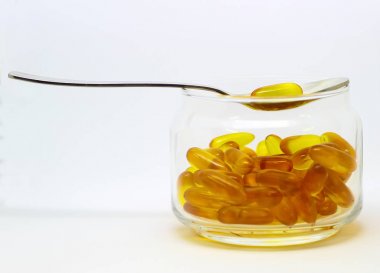 Morina karaciğer yağı omega 3 e vitamini jel kapsül şeffaf cam şişede beyaz arka plan üzerinde çelik bir kaşık ile izole