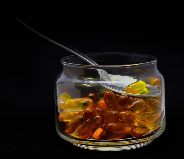 Kabeljaulebertran Omega-3-Vitamin-E-Gel-Kapseln isoliert auf schwarzem Hintergrund in einer transparenten Glasflasche mit Stahllöffel — Stockfoto