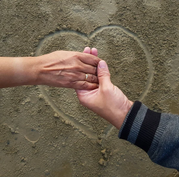 romantic couple on date holding hands on heart sign background drawn on wet beach sand