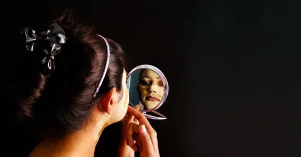 Uma senhora indiana com embalagem facial aplicada em condição semi-seca verificando seu rosto em um espelho com foco seletivo na imagem do espelho — Fotografia de Stock