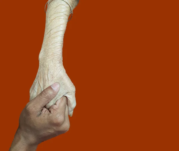 Рука пожилого человека, держащего руку молодой, пожилой концепции поддержки в оранжевом фоне — стоковое фото