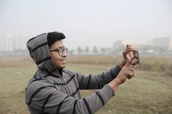 Мужчина щелкает фотографию со смартфона, одетый в зимние одежды и перчатки с акцентом на модели лица с туманным туманом на заднем плане . — стоковое фото