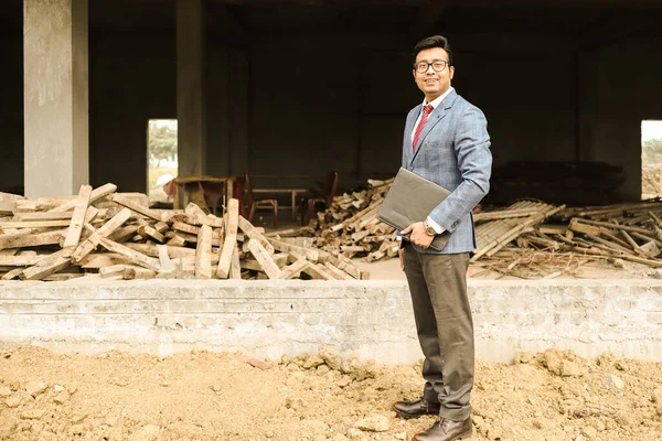 an engineer in formal suit and pant with portfolio near a construction site.