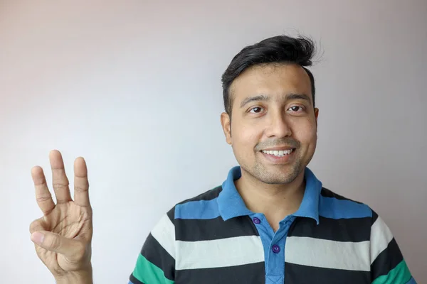 A young indian man confident and smiling indicating three symbol isolated in white background with copy space for text. — 스톡 사진