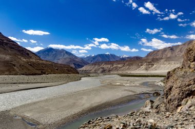 Eğri büğrü yol, yüksek yol ve manzara kayalık çakıl taşlarının ön planında parlak mavi gökyüzünü ve ladakh, Kaşmir 'in çorak kuru dağlarını gösteriyor.