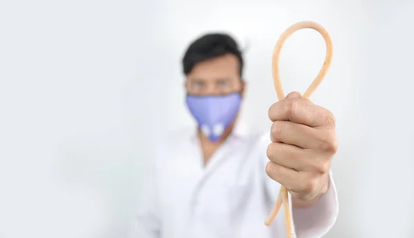 Un medico professionista in mantello bianco e maschera protettiva che tiene in mano un laccio emostatico con messa a fuoco selettiva in mano con sfondo sfocato — Foto Stock