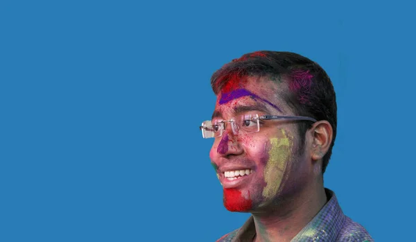 Side portrait of a young man with holi colours on face smiling a with isolated solid sky background — Stock Photo, Image