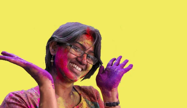 Portrait of a young lady with holi colours smiling at the camera with isolated solid yellow background — Stockfoto