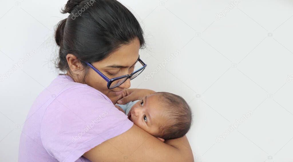 a young mother in spectacles looking at her infant baby boy in her lap in solid grey background with space for text. mothers day concept photo