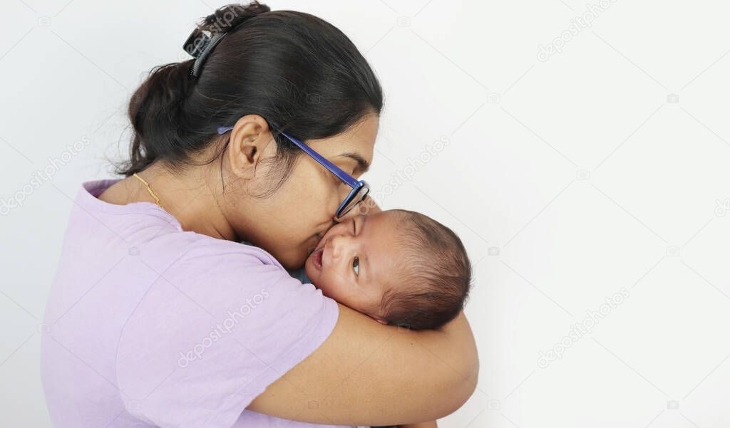 a young mother in spectacles kissing her infant baby boy in her lap in solid grey background with space for text. mothers day concept photo