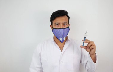 Beyaz önlüklü ve elinde şırınga tutan koruyucu maskeli bir tıp uzmanı.