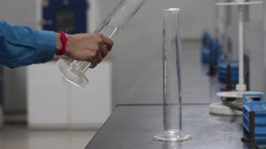 Kimya laboratuvarında siyah granit bir levhanın üzerindeki konik bir şişeye ölçüm silindirinden sıvı kimyasal dökülüyor.