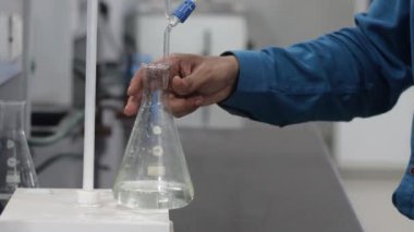 Burette altında konik matarada renksiz sıvı sallayarak titrasyon tepkisi