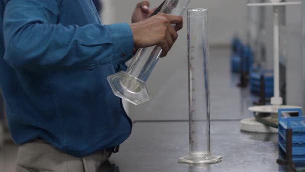 Pouring liquid chemical from a measuring cylinder to a conical flask on a black granite slab in chemistry laboratory — Stock Video