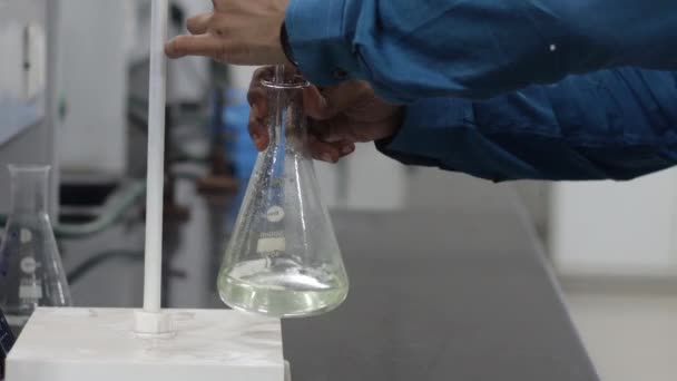 Titratiereactie door kleurloze vloeistof te schudden in een erlenmeyer onder een buret — Stockvideo