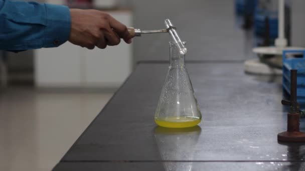 Kleurverandering van een gele chemische stof in een erlenmeyer na toevoeging van een witte chemische stof uit een reageerbuis in een chemisch laboratorium — Stockvideo