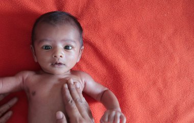 malnourished baby looking at the camera lying on orange red velvet cloth background. protein energy malnutrition concept image clipart