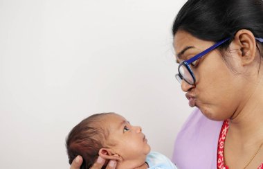 Bir anne, beyaz arka planda izole edilmiş bebeğine komik bir yüz ifadesi takınıyor.