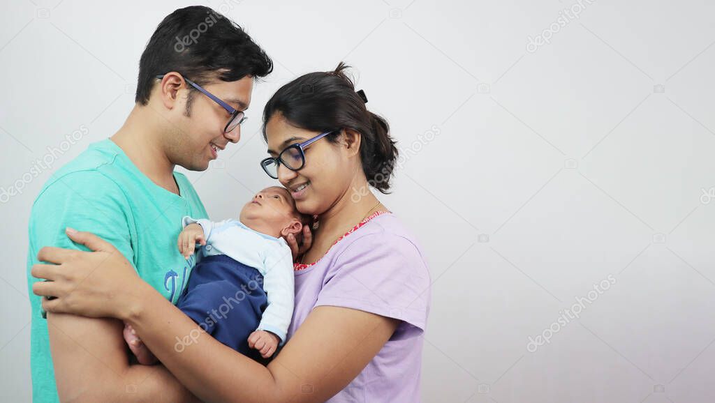 a young man with his wife and newborn kid looking at the baby isolated in white background