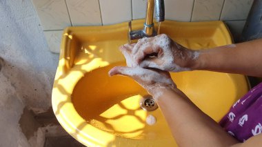 Her iki elini de sabunla yıkamak sarı bir lavabonun altında musluk suyuyla köpük ve köpük üretmek için.