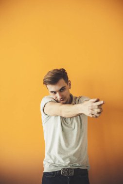 Yakışıklı çekici. Rahat kıyafet silah tutmak yakışıklı genç adam geçti ve üzerinde turuncu arka plan ayakta gülümseyen izole