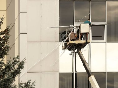 Bir kaldırma platformundaki iki işçi yüksek bir binanın dışındaki bir pencereyi tamir ediyorlar. Gökdelenlerin camlarını siliyorum. Yüksek irtifa çalışması tehlikesi. Gökdelenlerin onarımı ve bakımı