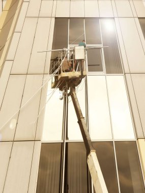 Bir kaldırma platformundaki iki işçi yüksek bir binanın dışındaki bir pencereyi tamir ediyorlar. Gökdelenlerin camlarını siliyorum. Yüksek irtifa çalışması tehlikesi. Gökdelenlerin onarımı ve bakımı