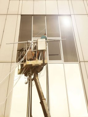 Bir kaldırma platformundaki iki işçi yüksek bir binanın dışındaki bir pencereyi tamir ediyorlar. Gökdelenlerin camlarını siliyorum. Yüksek irtifa çalışması tehlikesi. Gökdelenlerin onarımı ve bakımı