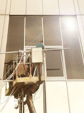 Bir kaldırma platformundaki iki işçi yüksek bir binanın dışındaki bir pencereyi tamir ediyorlar. Gökdelenlerin camlarını siliyorum. Yüksek irtifa çalışması tehlikesi. Gökdelenlerin onarımı ve bakımı