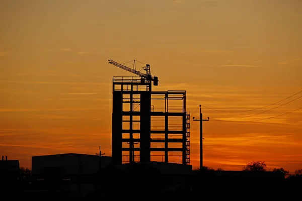用塔式起重机建造中的摩天大楼的骨架，与落日背景下的橙色天空相对照。 自然现象的浪漫风景。建筑 — 图库照片